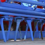 Denti curvi di un erpice rotante disposti in fila sotto il telaio blu della macchina