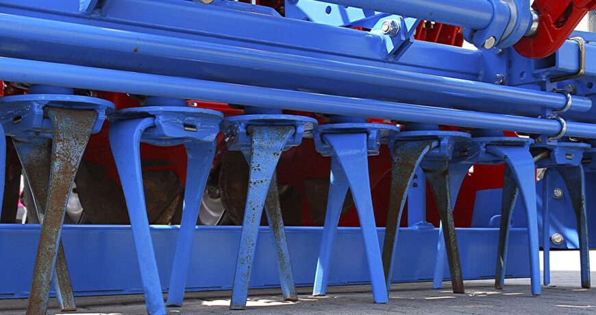 Denti curvi di un erpice rotante disposti in fila sotto il telaio blu della macchina